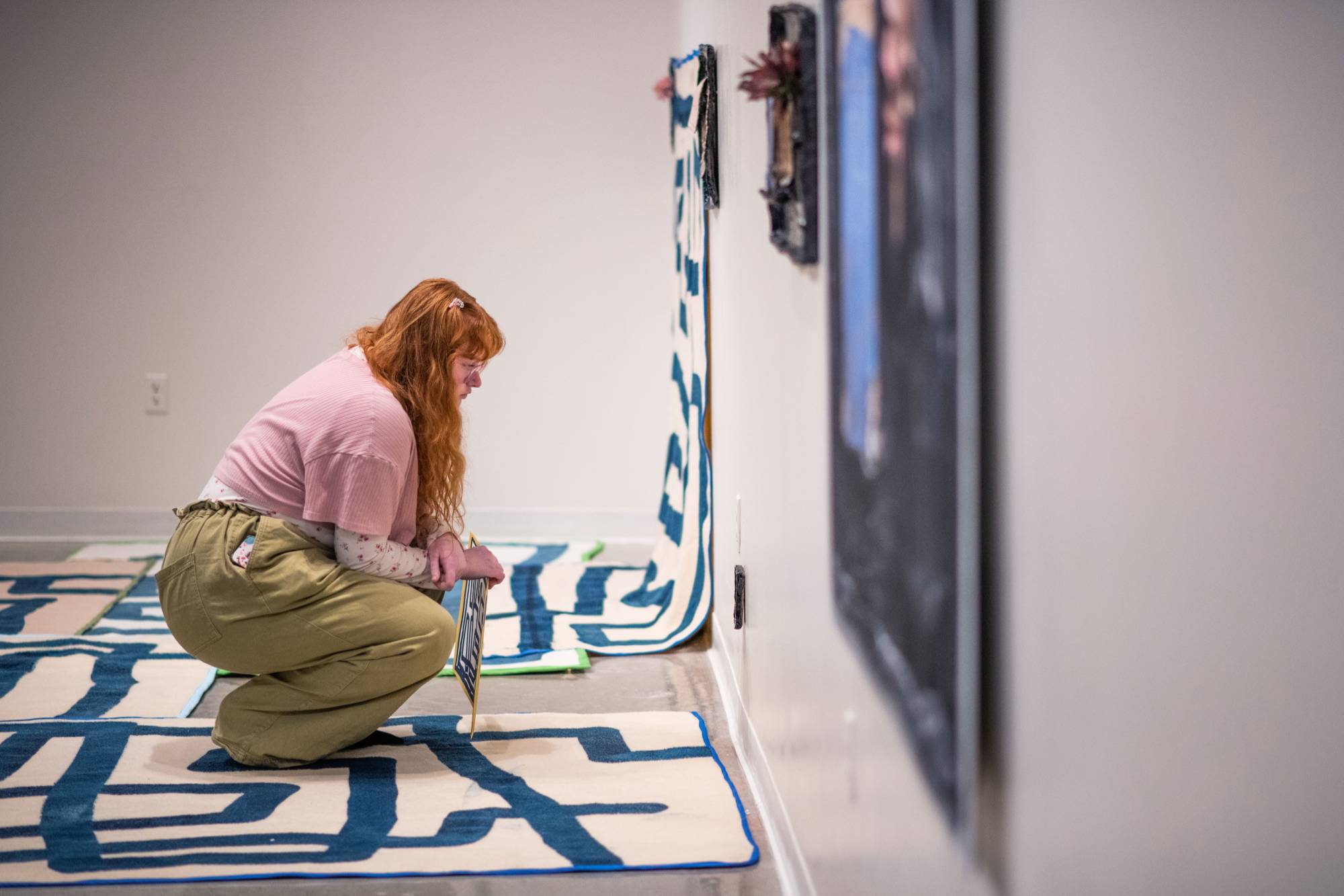 Visitor to the Padnos Gallery standing on an art installation by Emmy Bright, made up of wool rugs drawn on by a printmaking process to look like lines.